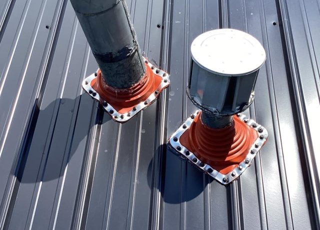 Two roof pipes in red flexible boots on metal flanges ringed with fasteners