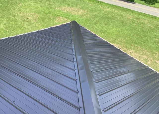 A hip cap running down a charcoal metal slope toward the roof corner, with a road beyond