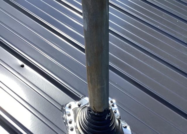 One older pipe in a black flexible boot on a metal flange, red boots behind it
