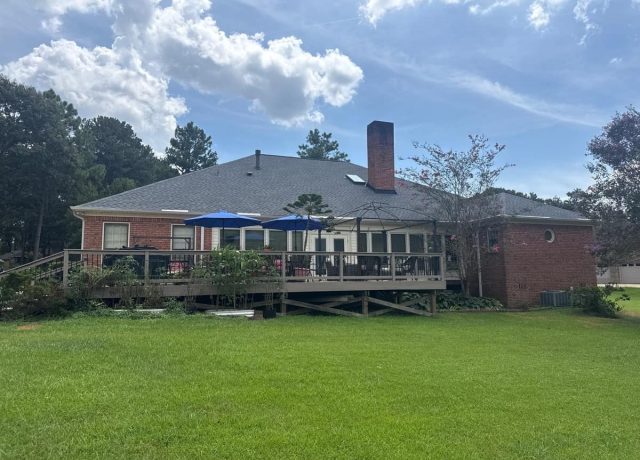 Back of the house with a gray hip roof, brick chimney, skylight and wooden deck