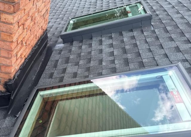 Brick chimney with dark flashing and two skylights set into gray shingles on the back slope