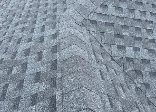 Cap shingles stacked in a chevron pattern down a hip, with a vent pipe in the distance