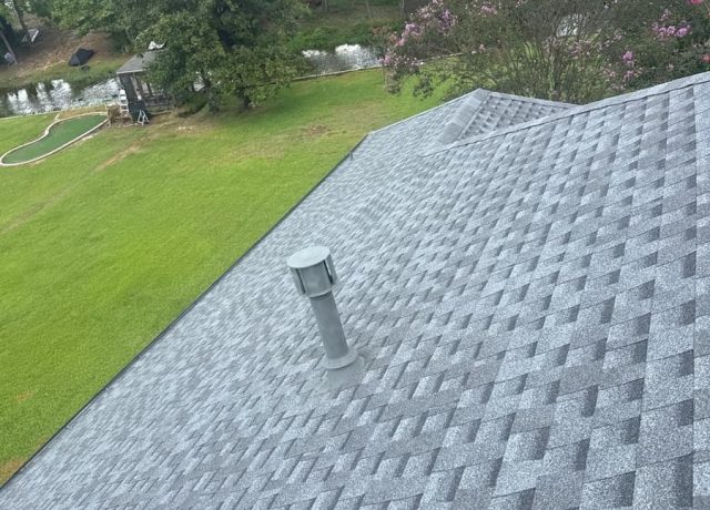 Gray vent stack on the new shingles, with a pond and a flowering tree behind the house