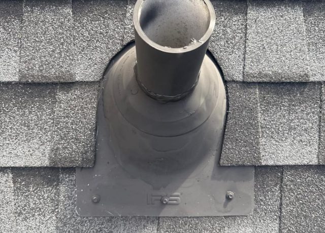 Gray molded pipe boot flat on the shingles, sealant ring at the pipe, two fasteners
