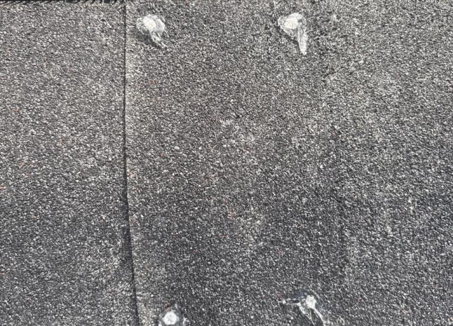 Cap shingle across a black ridge vent strip with clear sealant over four fasteners