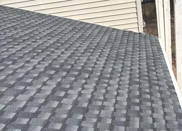 Gray shingle rows meeting cream vinyl siding, with white porch columns at the right edge